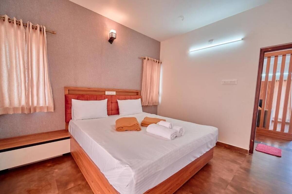 A hotel room with a wooden bed, white linens, a nightstand, and a wall-mounted light fixture.