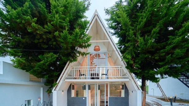 A modern, triangular-shaped building with a balcony, surrounded by trees.