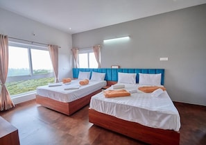 Ett hotellrum med två sängar, ett trägolv, ett stort fönster med gardiner och en blå sänggavel.