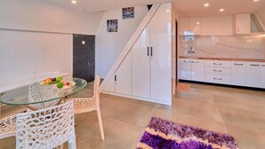 A modern kitchen with white cabinets, a glass dining table, and a purple rug.