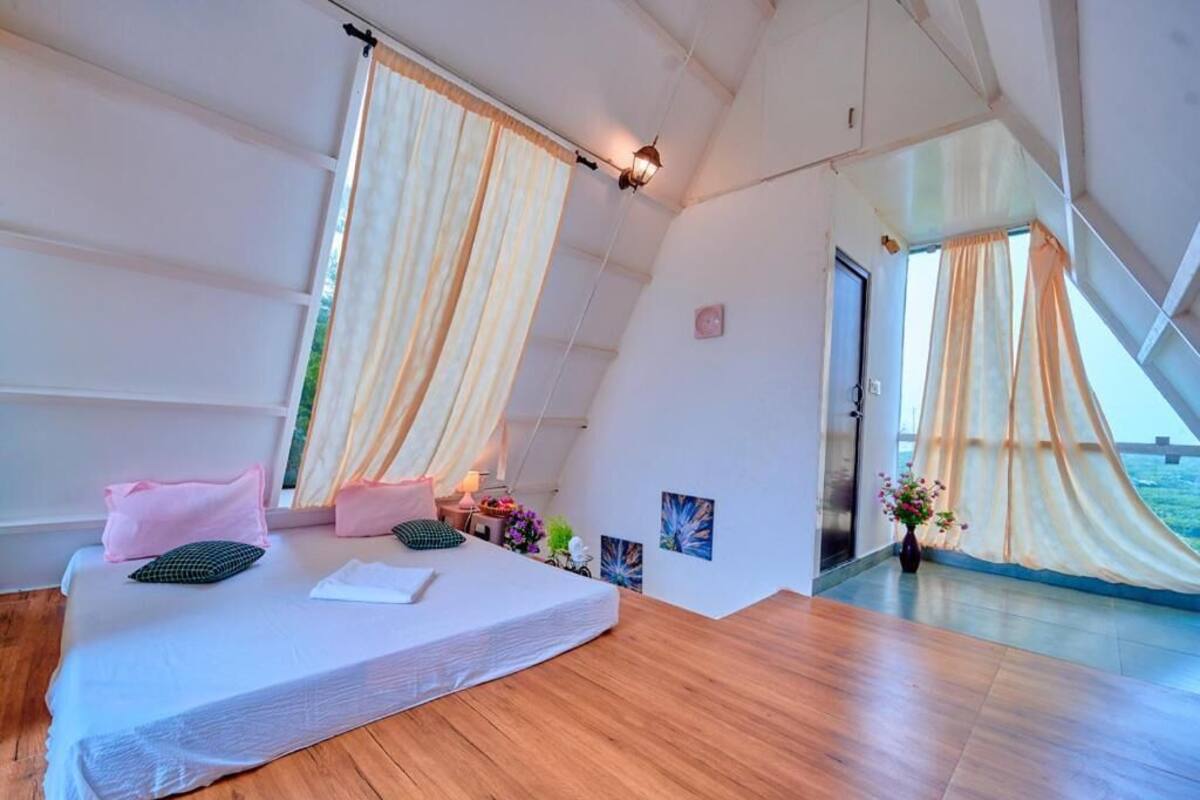 A bedroom with a bed, curtains, a nightstand, a lamp, and a view of the sea.