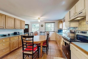 A kitchen with wooden cabinets, a dining table with chairs, a ceiling fan, and a window with blinds.