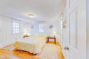 A bedroom with a large bed, two bedside tables, a window, and a door. - Duplex bungalows with fast WiFi, enclosed yard, & walkable locale, dog-friendly (West Yarmouth)