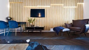 Una sala de estar moderna con un televisor de pantalla plana montado en una pared de madera, un suelo de madera oscura, un sofá azul, un sillón de cuero marrón y una pequeña mesa con una planta.