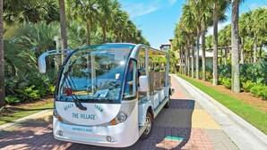 A white bus with 'The Village' and 'Beach' written on it, parked on a paved path surrounded by palm trees. - Resting BeachFace + Private Beach, Bikes & Games (Inlet Beach)