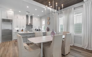 A modern kitchen with white cabinets, a stainless steel refrigerator, and a dining area with a table and chairs. - Resting BeachFace + Private Beach, Bikes & Games (Inlet Beach)