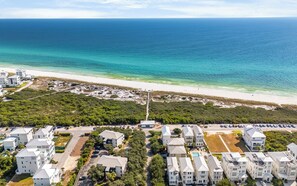 Vista aérea de una zona residencial costera con propiedades frente al mar, una playa de arena y una vista despejada del océano.