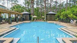A rectangular swimming pool with a wooden deck surrounding it, shaded by umbrellas, and a wooden pergola on one side. - Resting BeachFace + Private Beach, Bikes & Games (Inlet Beach)