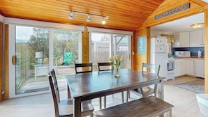 Een houten plafond, een eettafel met stoelen, een keukenhoek en een schuifdeur naar buiten.