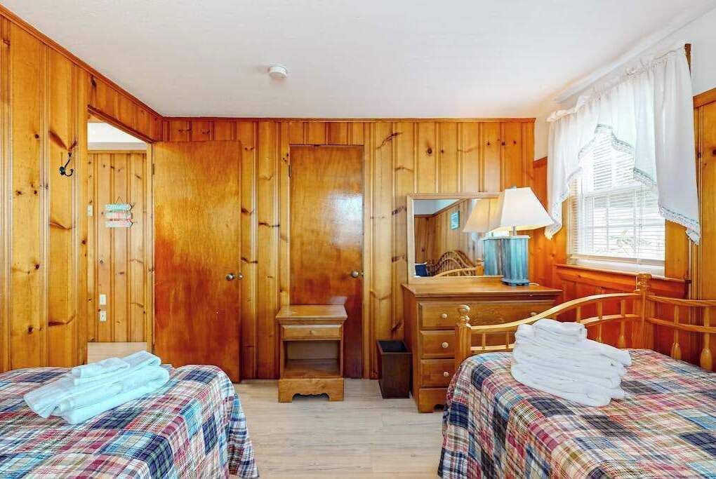 A wooden-paneled room with two beds, a desk, and a mirror.