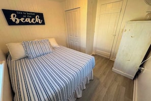Un dormitorio con colcha a rayas, un letrero en la pared y un armario blanco.