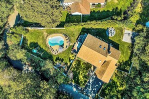 An aerial view of a property with a swimming pool, a large house, and surrounding greenery. - Spacious coastal retreat with heated pool, kayaks, game room & pond views (Centerville)