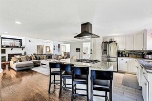 A modern kitchen with white cabinets, a central island, and a stainless steel range hood. - Spacious coastal retreat with heated pool, kayaks, game room & pond views (Centerville)