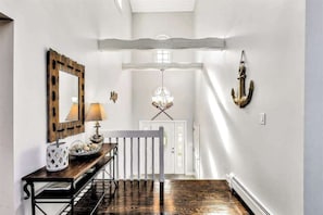 A hallway with a wooden bench, a mirror, a chandelier, and a coat rack. - Spacious coastal retreat with heated pool, kayaks, game room & pond views (Centerville)
