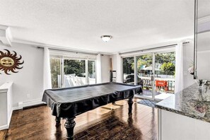 A pool table in a room with large windows and a view of the outdoors. - Spacious coastal retreat with heated pool, kayaks, game room & pond views (Centerville)