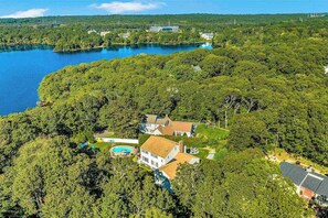A large house surrounded by dense forest with a swimming pool and a view of a lake. - Spacious coastal retreat with heated pool, kayaks, game room & pond views (Centerville)