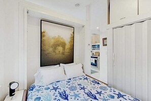 A bedroom with a bed, a nightstand, a painting, and a view into the kitchen. - Stylish seaside escape with harborview rooftop deck, patio & steps to nightlife (Provincetown)