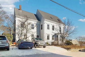 A two-story house with a garage, parked cars, and a clear sky. - Stylish seaside escape with harborview rooftop deck, patio & steps to nightlife (Provincetown)
