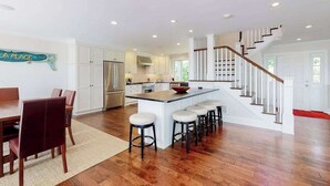 A spacious kitchen with a central island, white cabinetry, and a wooden staircase. - Luxe lakefront home on Follins Pond with private beach, amazing decks & yard (Yarmouth Port)
