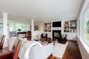 A spacious living room with a fireplace, bookshelves, and a television. - Luxe lakefront home on Follins Pond with private beach, amazing decks & yard (Yarmouth Port)