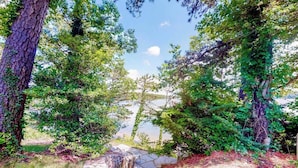 A stone pathway leading through a forested area with a lake in the background. - Luxe lakefront home on Follins Pond with private beach, amazing decks & yard (Yarmouth Port)