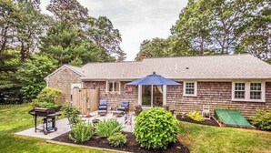 Una casa con un patio, mobiliario exterior y una parrilla.