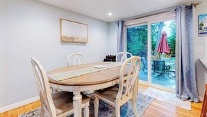 Un comedor con mesa y sillas de madera, un cuadro en la pared y vistas a un patio exterior con un paraguas rosa.
