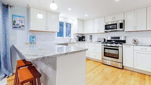 Una cocina moderna con armarios blancos, una isla central con taburetes, horno empotrado y microondas.