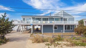 A two-story beach house with a balcony, a covered porch, and a sandy driveway. - Lovely home with private pool, hot tub, foosball, air hockey & easy beach access (Virginia Beach)