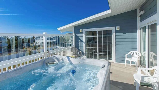 A hot tub on a deck with a view of houses, a sliding glass door, and white plastic chairs. - Lovely home with private pool, hot tub, foosball, air hockey & easy beach access (Virginia Beach)
