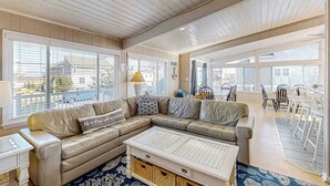 A spacious living room with a large sectional sofa, a coffee table, and a dining area with chairs and a table. - Lovely home with private pool, hot tub, foosball, air hockey & easy beach access (Virginia Beach)