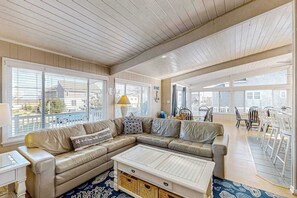 A spacious living room with a large sectional sofa, a coffee table, and a dining area with chairs and a table. - Lovely home with private pool, hot tub, foosball, air hockey & easy beach access (Virginia Beach)