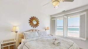 Een slaapkamer met een bed, een plafondventilator, een spiegel in zonnestraalvorm en uitzicht op het strand.