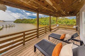 Eine überdachte Terrasse mit Holzbalkonen, zwei Liegestühle mit Kissen und Blick auf See und Wald.