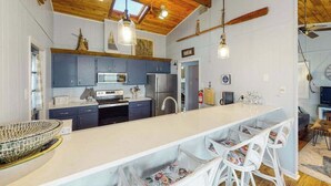 A modern kitchen with blue cabinets, a white island, and hanging pendant lights. - Remodeled, ocean view home with rooftop deck & fast WiFi - dog-friendly (Virginia Beach)