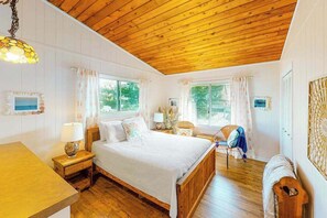 Ein Schlafzimmer mit Holzbalkendecke, einem Bett, einem Nachttisch, einem Stuhl und einem Fenster.