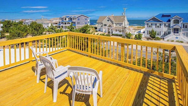A wooden deck with chairs, overlooking a residential area with houses and a beach. - Remodeled, ocean view home with rooftop deck & fast WiFi - dog-friendly (Virginia Beach)