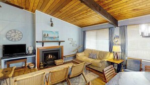 A cozy living room with a fireplace, a television, wicker furniture, and a clock on the wall. - Remodeled, ocean view home with rooftop deck & fast WiFi - dog-friendly (Virginia Beach)