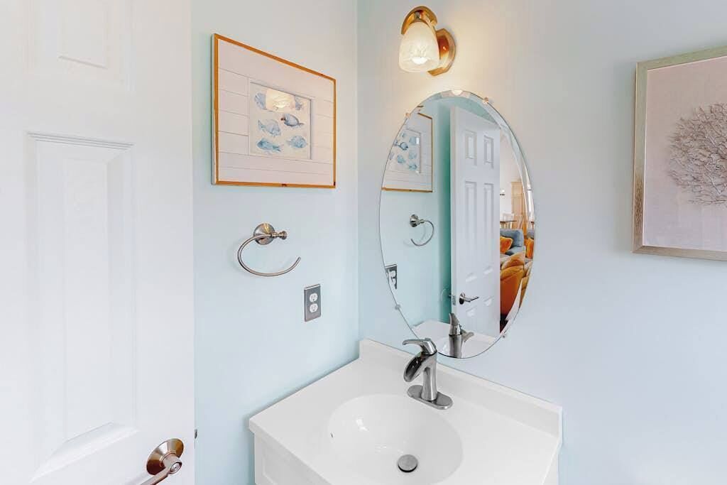 Een badkamer met een witte wastafel, een grote spiegel, een lijst met een foto en een wandlamp.