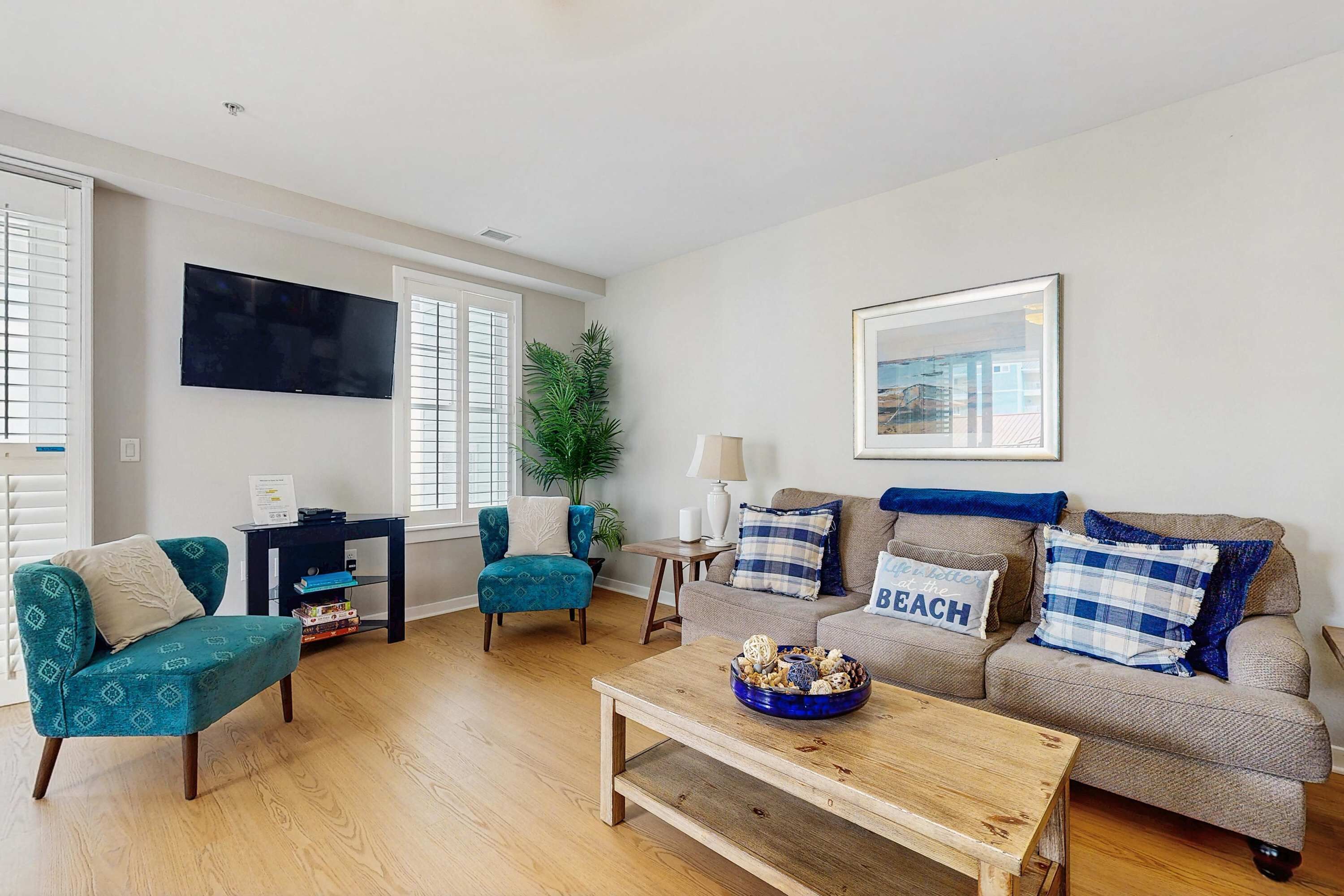 A living room with a sofa, armchair, coffee table, and a TV mounted on the wall.