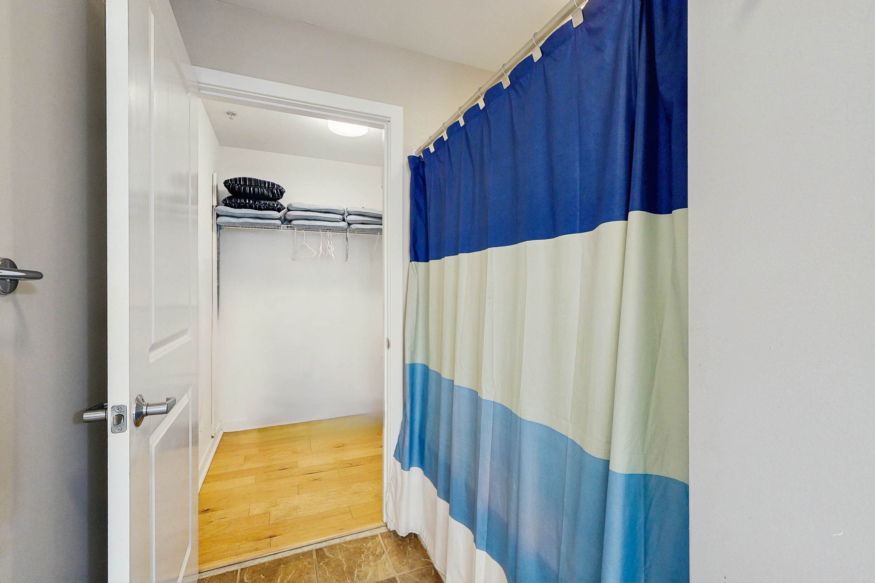 A bathroom with a shower curtain, a towel rack with folded towels, and a wooden floor.