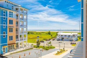 Un immeuble à plusieurs étages doté de balcons, d’un parking et offrant une vue sur un champ verdoyant et une étendue d’eau.