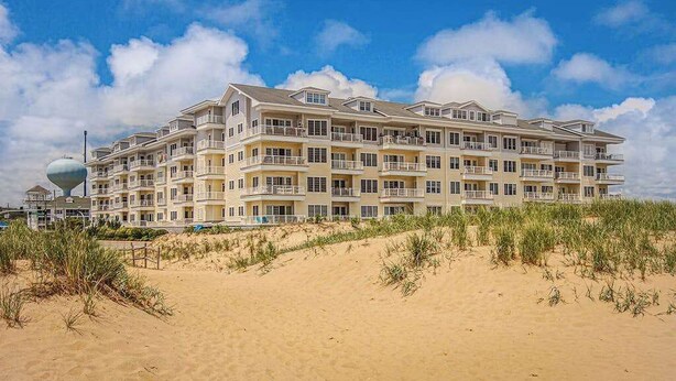 Ein mehrstöckiges Hotel mit Balkonen, gelegen an einem Sandstrand bei blauem Himmel.