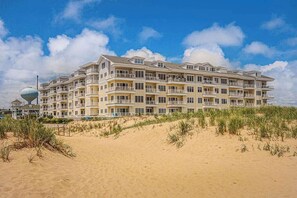 Un hôtel à plusieurs étages doté de balcons, situé sur une plage de sable fin, sous un ciel dégagé.