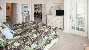 Ein Schlafzimmer mit Bett, Kommode, Fernseher und einer Tür zu einem Essbereich.