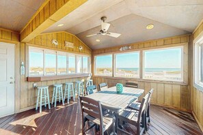 A wooden deck with a table and chairs, a ceiling fan, and large windows with a view of the beach. - Spacious oceanfront house w/beach access, decks, grill & free WIFI (Virginia Beach)