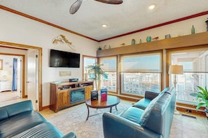 A spacious living room with a sofa, a coffee table, a TV, and a large window with a view. - Spacious oceanfront house w/beach access, decks, grill & free WIFI (Virginia Beach)