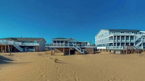 Ein Strandhotel mit mehreren Gebäuden, darunter ein großes mit Balkonen und ein kleineres mit einer Treppe zu einer Terrasse.