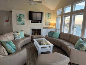 A living room with a fireplace, a ceiling fan, and large windows. - Sunlit 3-story home with private in-ground pool, balcony, washer/dryer (Virginia Beach)
