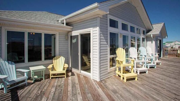Une maison dotée d’une terrasse couverte, de nombreuses fenêtres et d’un espace salon extérieur.